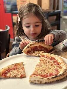 Young girl enjoying a slice of pizza in a cozy restaurant setting.