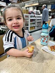Child enjoying a snack with a smile in a bakery setting.