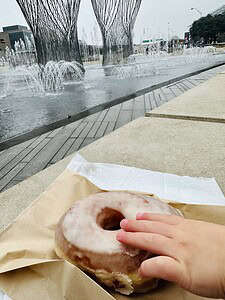 Delicious glazed donut resting on paper, with a child's hand about to take a bite, set against a cit.