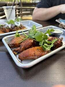 Grilled chicken wings garnished with fresh cilantro on a metal tray, served outdoors at The Migoni K.