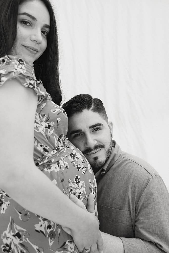 Expecting couple celebrating pregnancy, holding belly, smiling.